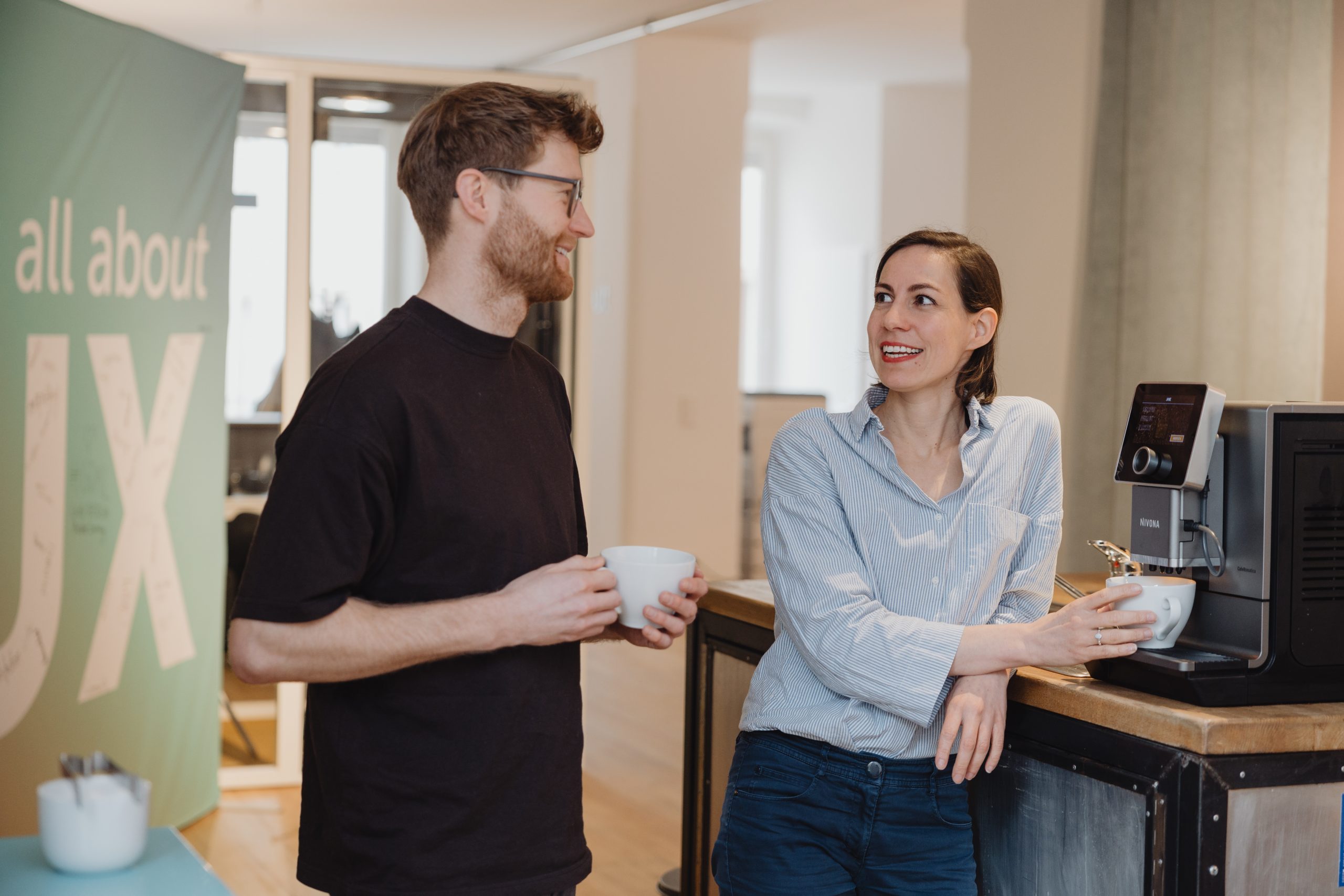 2 junge Leute quatschen bei der Kaffeemaschine.
